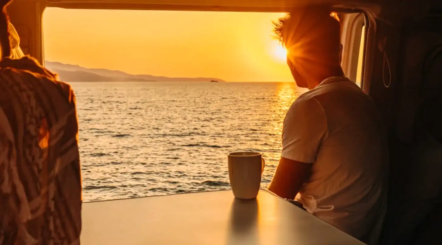 Man in camper looking at a sunrise over the ocean